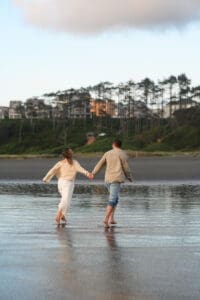 A couple walking hand-in-hand through shallow ocean water during their Seabrook Washington engagement session on the beach before their Mt Rainier elopement.