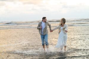 A couple walking hand-in-hand through shallow ocean water during their Seabrook Washington engagement session on the beach before their Mt Rainier elopement.